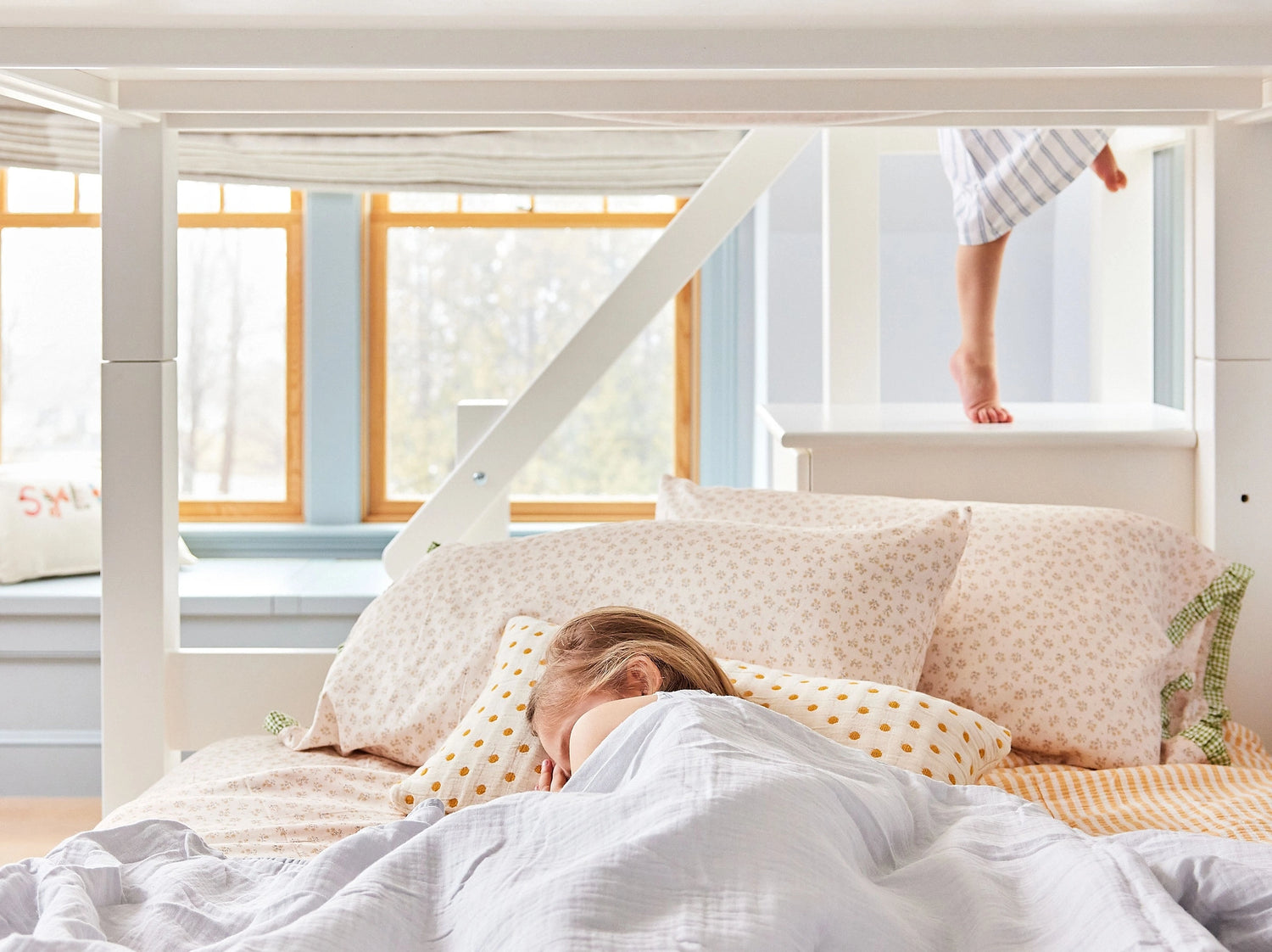 A little girl sleeps in the bottom bunk of a white twin over twin bunk bed.