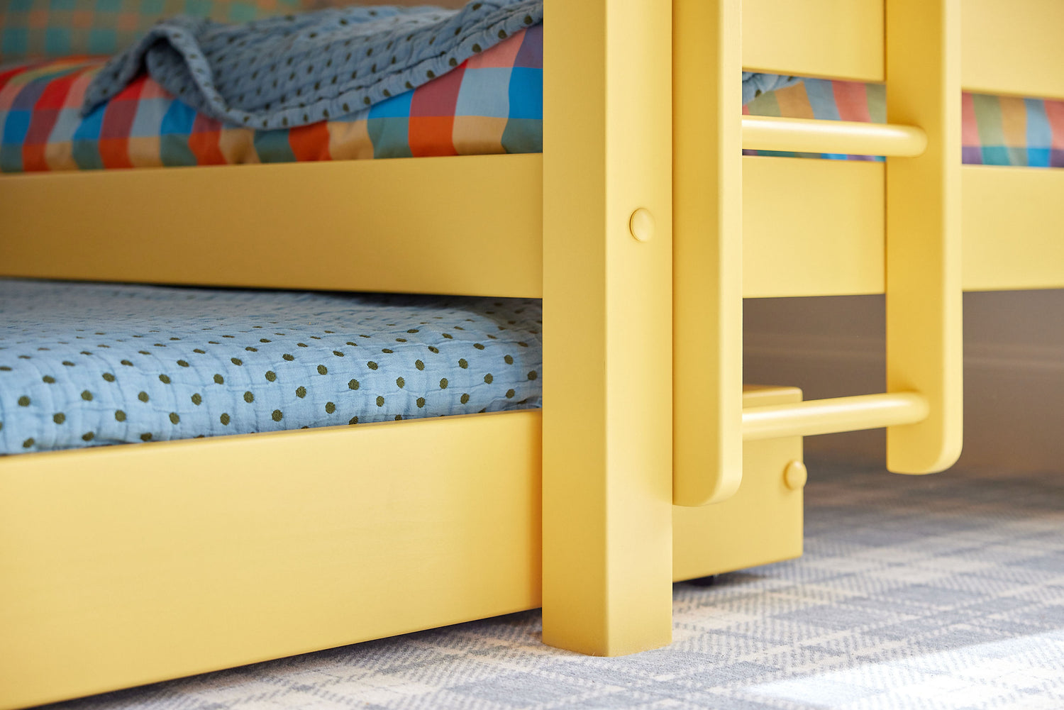 Closeup of a trundle mattress beneath a bright yellow bunk bed.