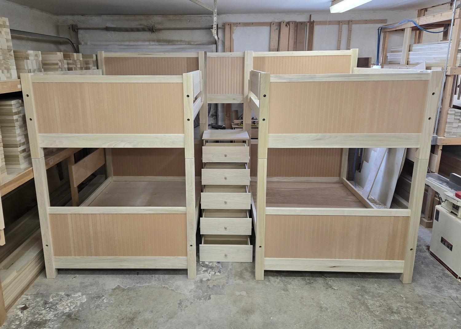 A view from the Maine Bunk Beds woodshop showing a two unpainted twin over twin bunk beds with stairs with drawers in between them.