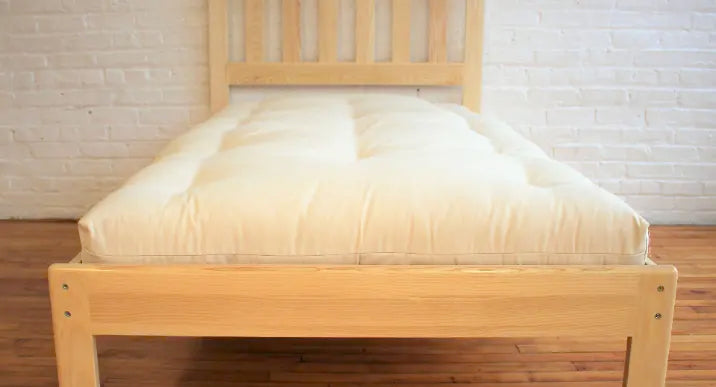 A handmade cotton and wool mattress on a simple wood platform bed.